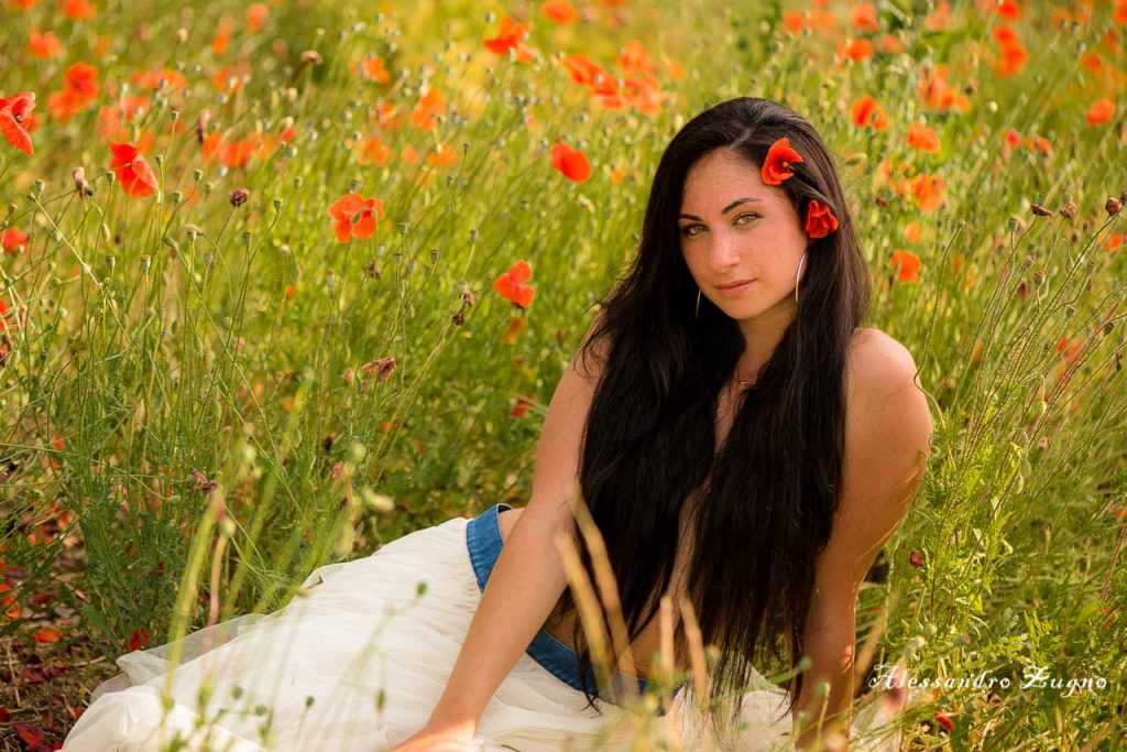 foto di ragazza con capelli che le coprono il seno circondata dai papaveri rossi